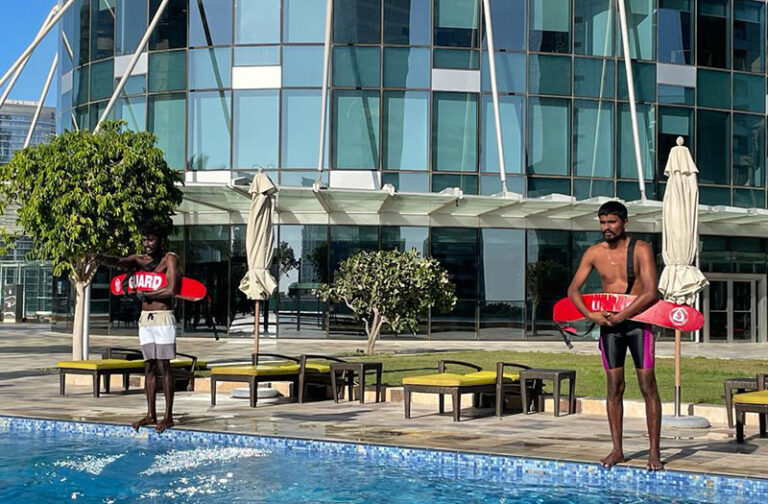 Two men with surfboards standing next to a pool.