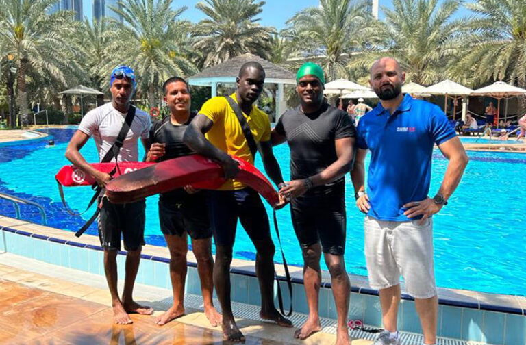 A group of men posing next to a swimming pool during Lifeguard Certification training.